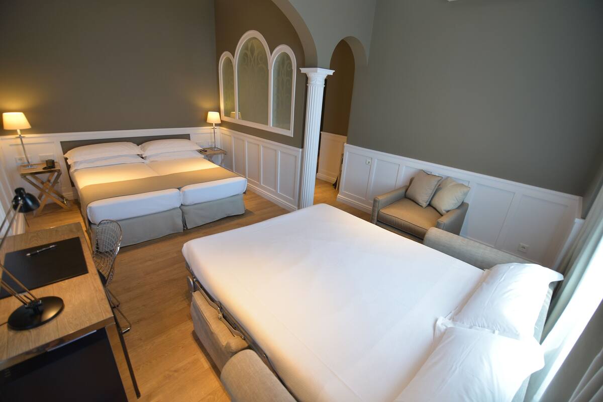 Una habitación de hotel con una cama grande, un sofá, un escritorio con lámpara y una ventana.