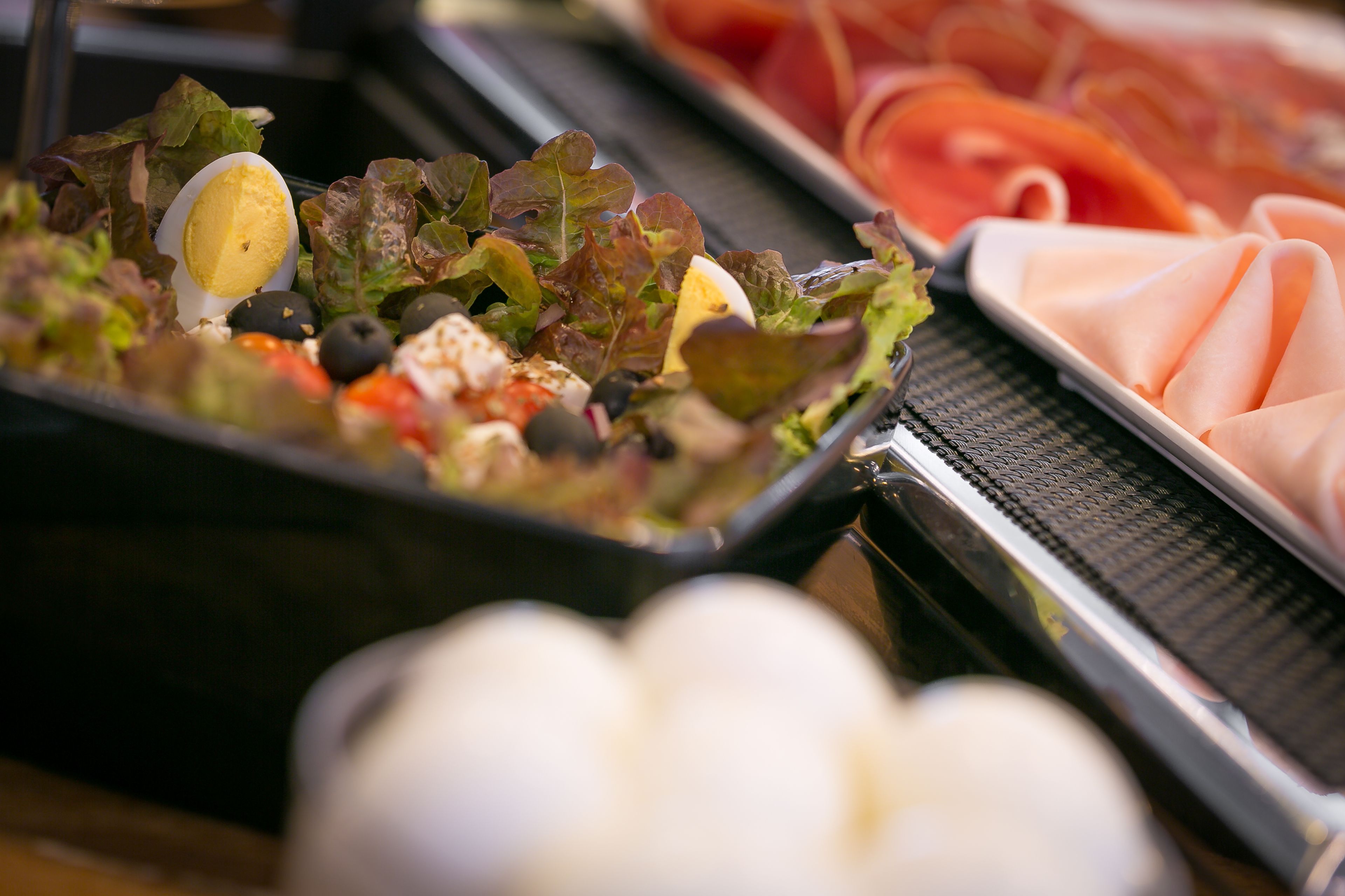 A buffet with a variety of food options including a salad, sliced meats, and a boiled egg.