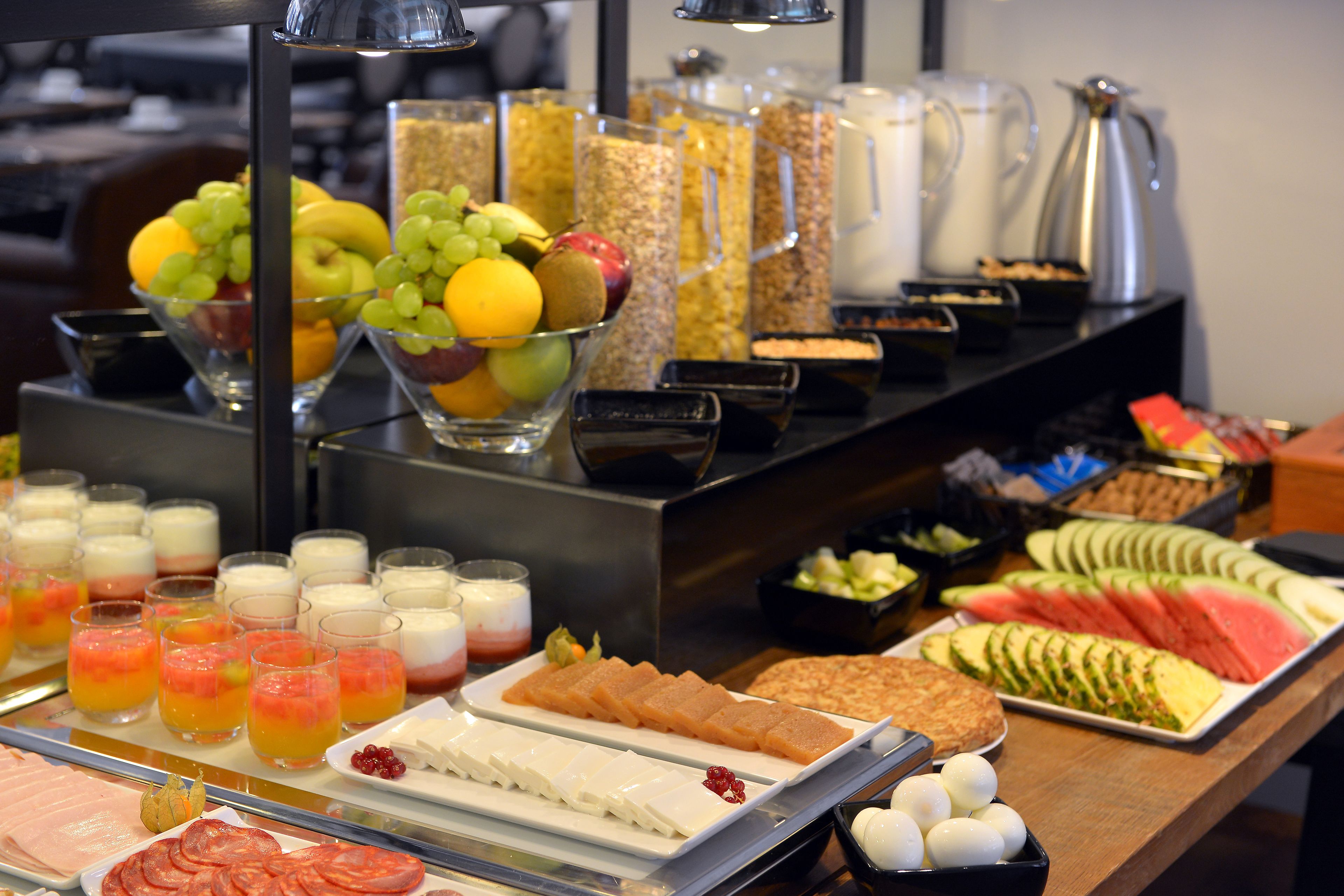 Buffet com diversos alimentos, incluindo frutas, queijos e carnes fatiadas.