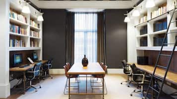 Una biblioteca con una mesa central, sillas, computadoras y estanterías.