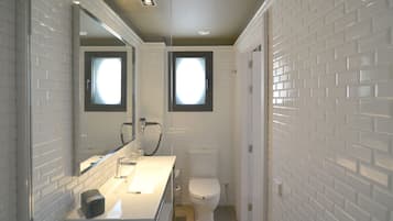Un baño con azulejos blancos tipo metro, un lavamanos blanco, un espejo y un inodoro.