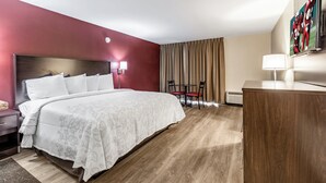 A hotel room with a bed, bedside table, lamp, and a desk with a chair. - Red Roof Inn PLUS+ & Suites Houston - IAH Airport SW (Houston)