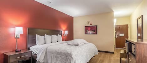 A hotel room with a bed, bedside tables, a nightstand, a wall-mounted lamp, a framed picture, and a wooden cabinet.