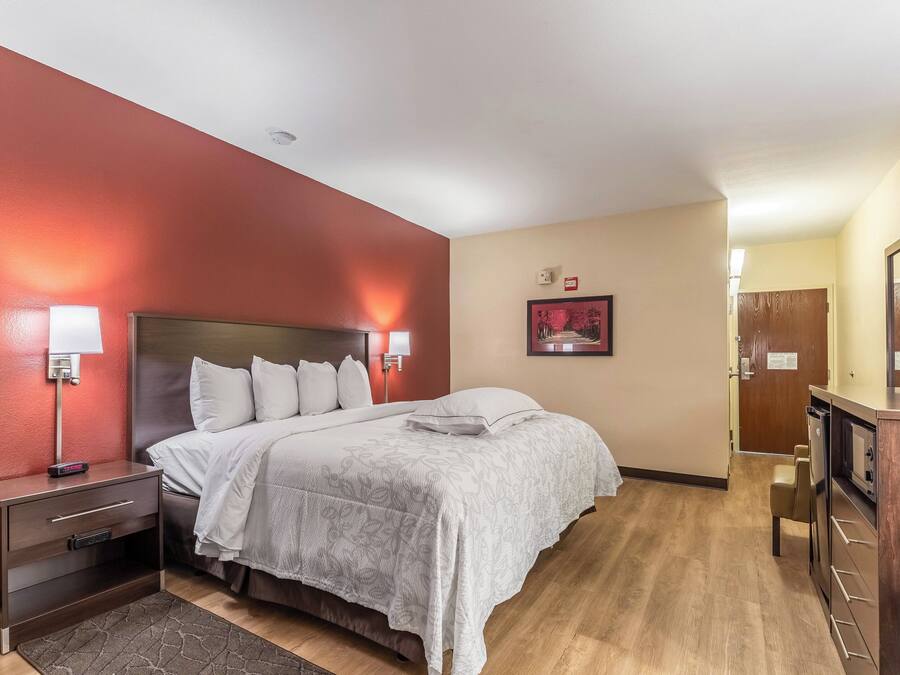 Una habitación de hotel con cama, mesitas de noche, una lámpara de pared, un cuadro enmarcado y un armario de madera.
