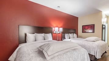 A hotel room with two beds, a red accent wall, and a painting.