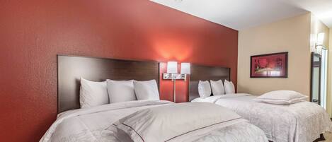 Habitación de hotel con dos camas, una pared de acento roja y un cuadro.