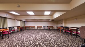 A conference room with multiple tables and chairs, carpeted floor, and ceiling lights. - Red Roof Inn PLUS+ & Suites Houston - IAH Airport SW (Houston)