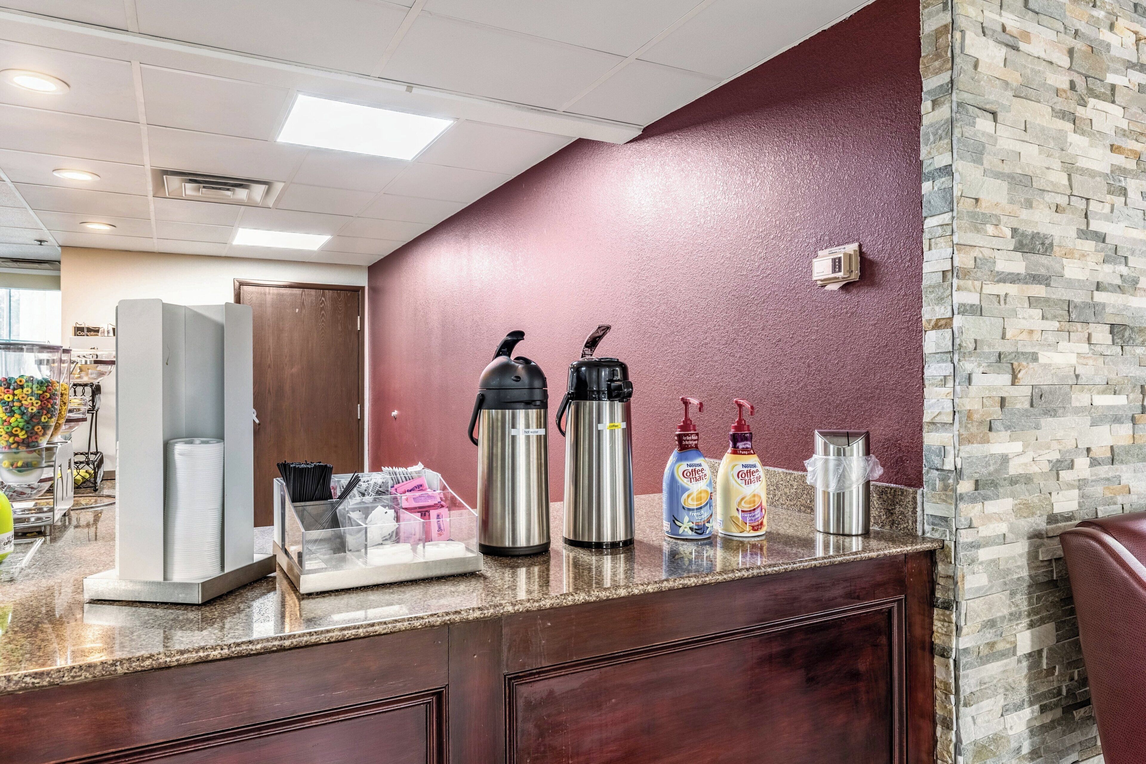 A coffee station with two hot water dispensers, a coffee maker, and two coffee dispensers on a counter.