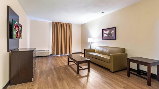 A hotel room with a flat-screen TV, a sofa, a coffee table, a lamp, and a picture on the wall. - Red Roof Inn PLUS+ & Suites Houston - IAH Airport SW (Houston)