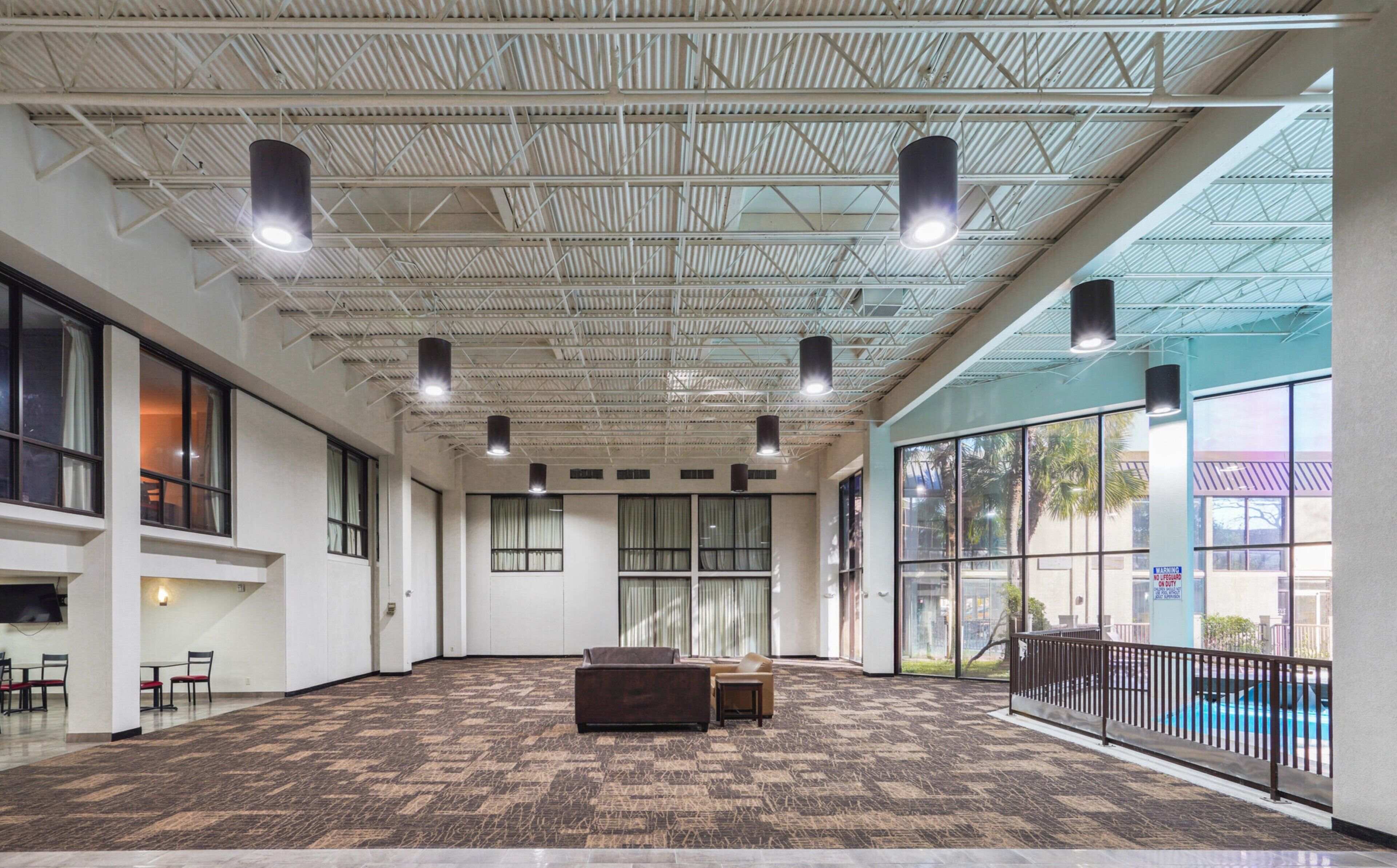 A spacious indoor area with a high ceiling, large windows, and a patterned carpet.