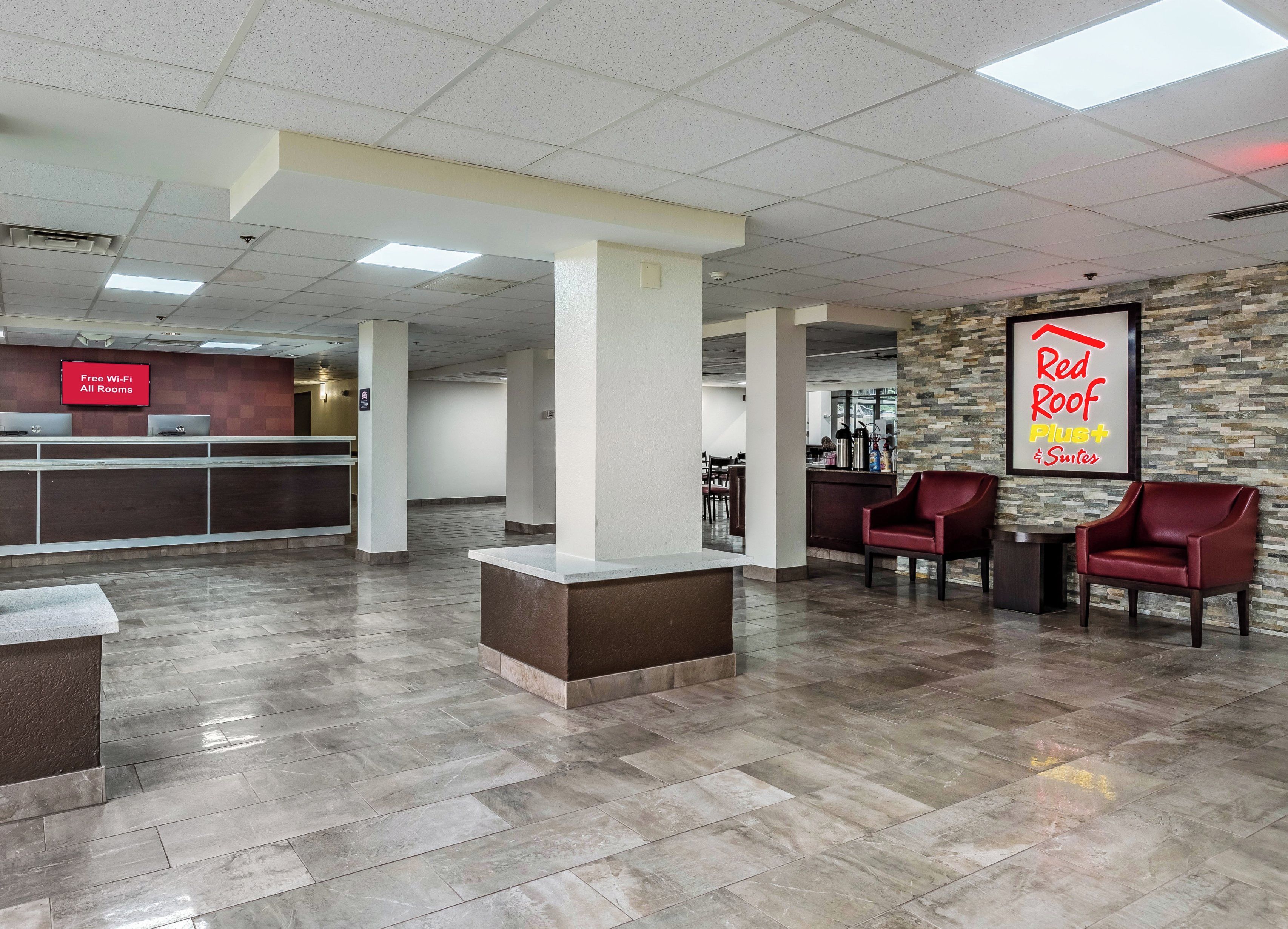 A hotel lobby with a reception desk, seating area, and a sign for Red Roof Plus Suites.