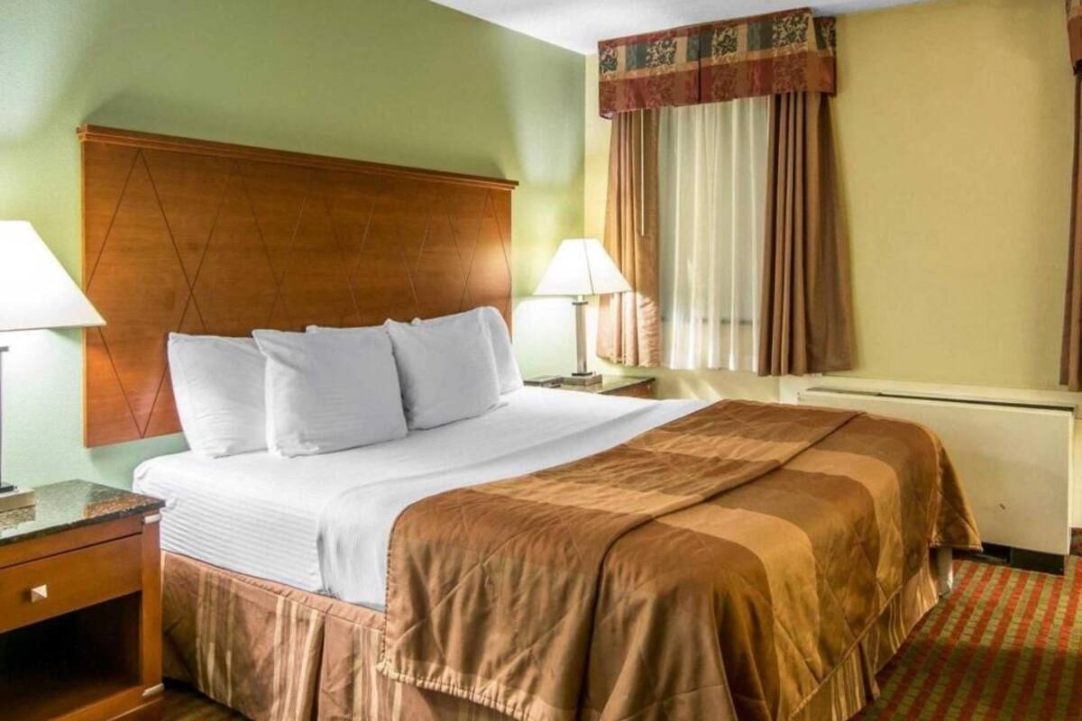 Una habitación de hotel con cama, dos mesitas de noche, una ventana con cortinas y un radiador.