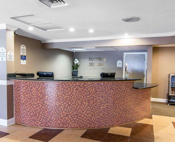 A hotel reception area with a check-in counter, a sign for 'ManStay Suites by Choice Hotels', and a door to the right.