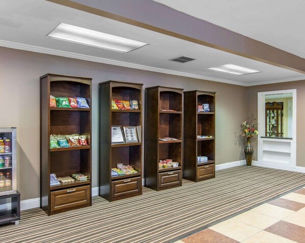 A lobby with three wooden bookcases filled with snacks and beverages, a small refrigerator, and a patterned carpet.