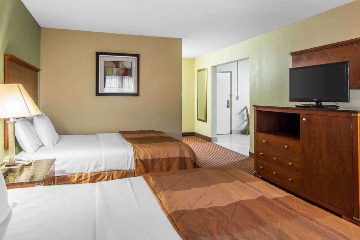 Habitación de hotel con dos camas, una televisión, un escritorio con lámpara y un cuadro enmarcado en la pared.