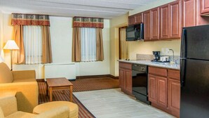 Une chambre d’hôtel compacte comprenant un coin cuisine, un canapé, une petite table et une fenêtre avec des rideaux.