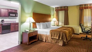 Une chambre d’hôtel comprenant un lit, des lampes de chevet, un bureau avec un téléphone, une chaise et une kitchenette équipée d’un four à micro-ondes.