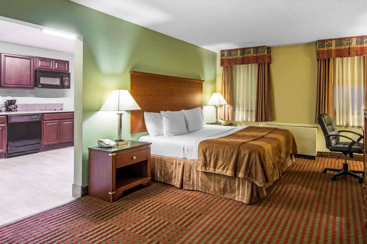 Habitación de hotel con cama, lámparas de noche, escritorio con teléfono, silla y kitchenette con microondas.