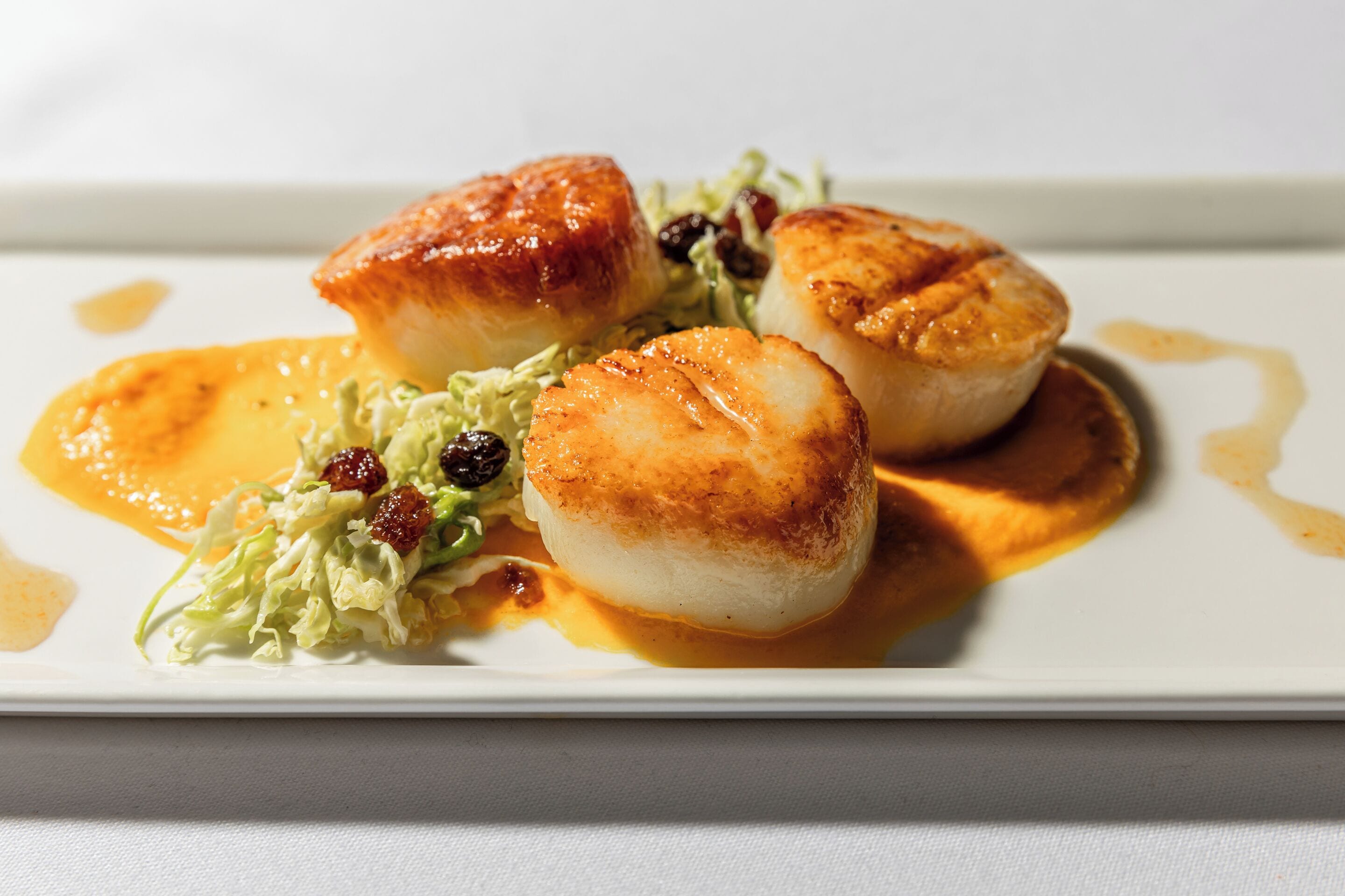 A plate with seared scallops, a dollop of sauce, and a side of greens.