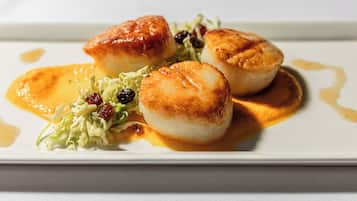 A plate with seared scallops, a dollop of sauce, and a side of greens.