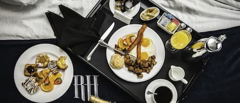 Ein Frühstücksbrett mit verschiedenen Backwaren, Eiern, Speck und Getränken auf einem Bett.