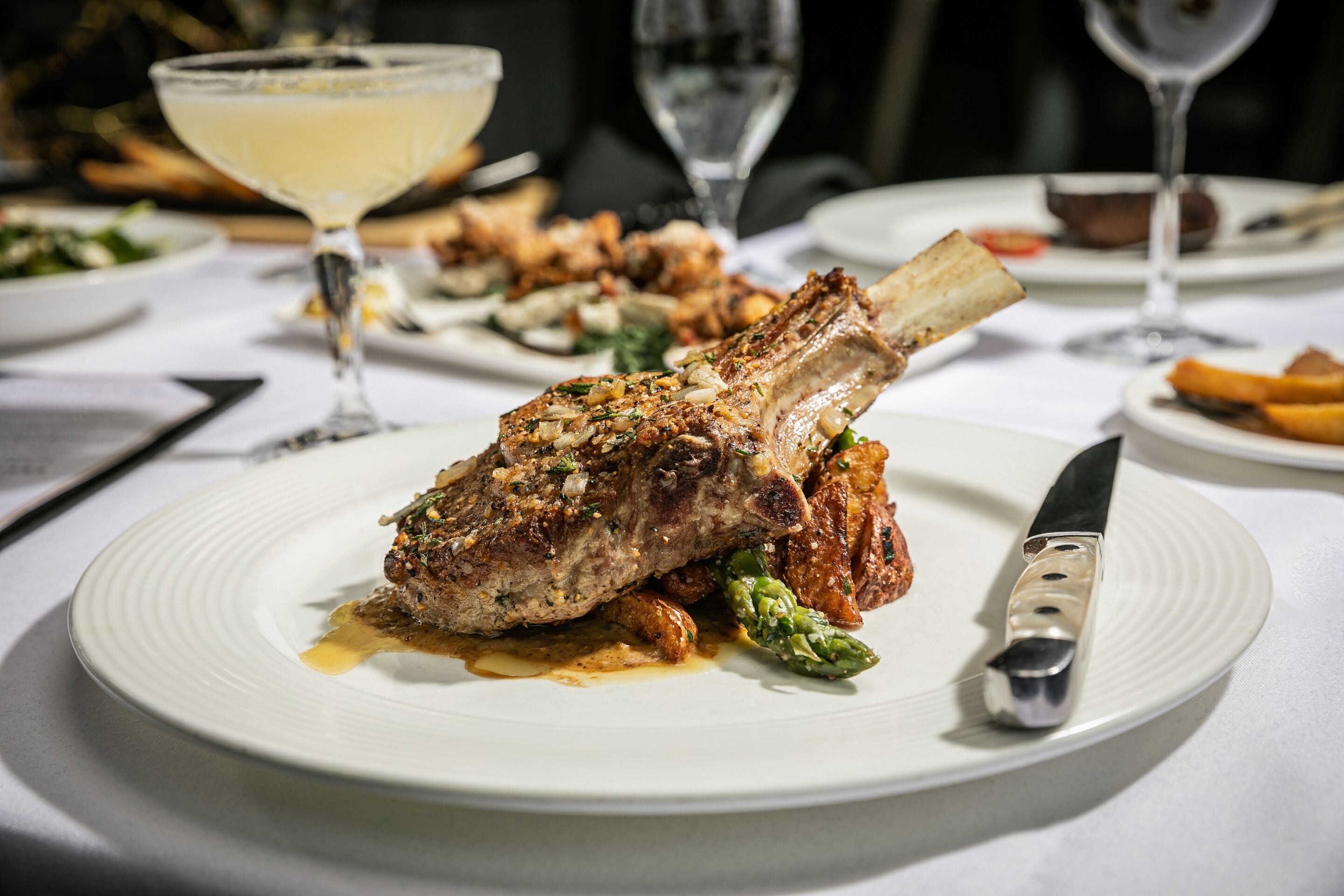 A plate of food with a lamb shank, asparagus, and sauce.