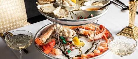 A seafood platter with various types of seafood, including oysters, shrimp, and lobster, served on ice with lemon wedges and condiments.