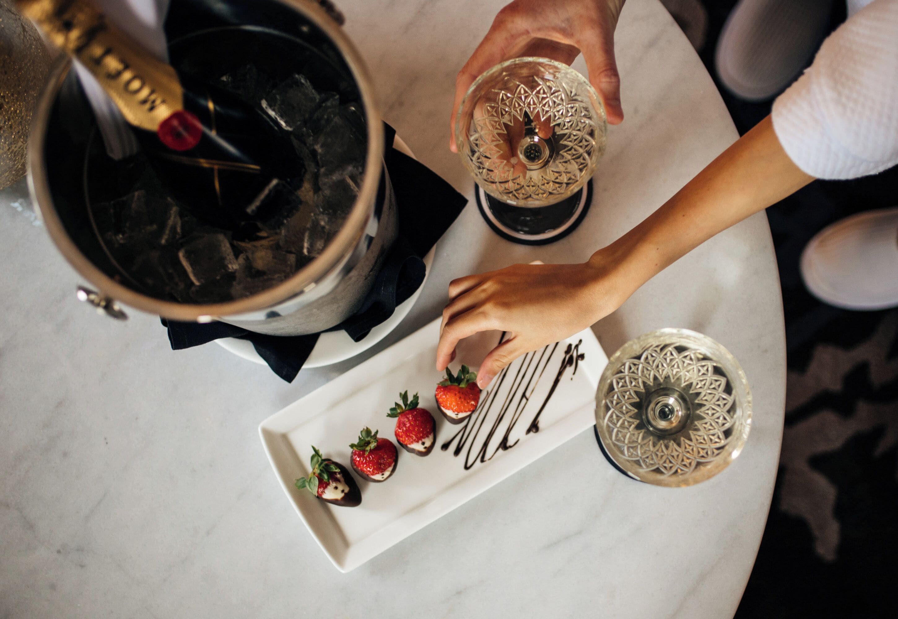 A person pouring a drink into a glass, a plate with strawberries, and a decorative bowl on a table.
