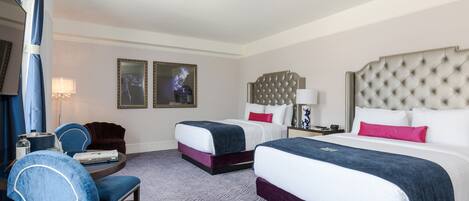 A hotel room with two beds, a desk with a chair, and a large window.