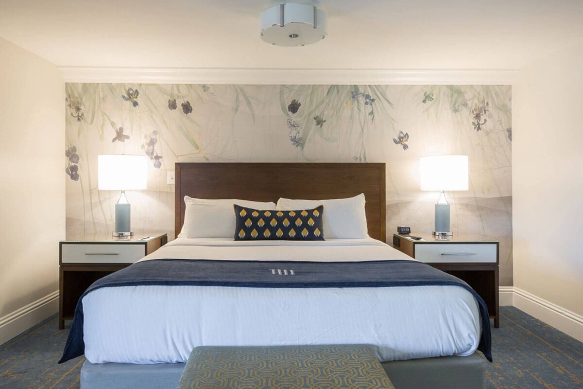 A hotel room with a large bed, two bedside tables, a headboard, and a floral wallpaper design.
