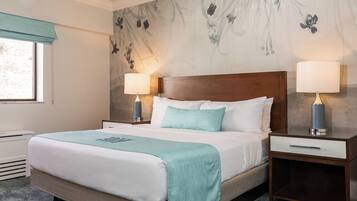Een opgemaakt bed met een blauwgroene plaid, twee bedlampjes en een nachtkastje met een lade.