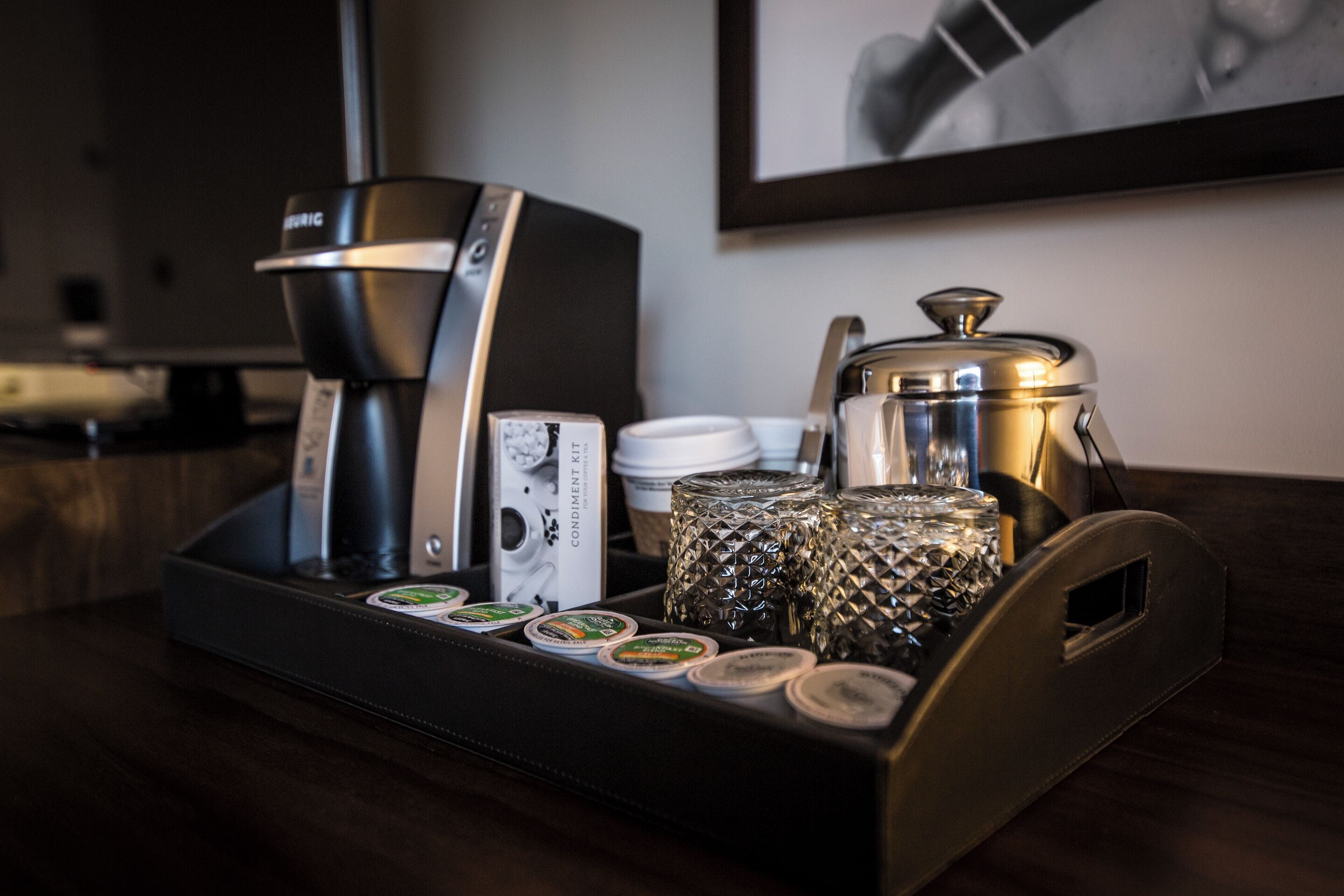 A coffee station with a coffee maker, cups, and condiments on a tray.
