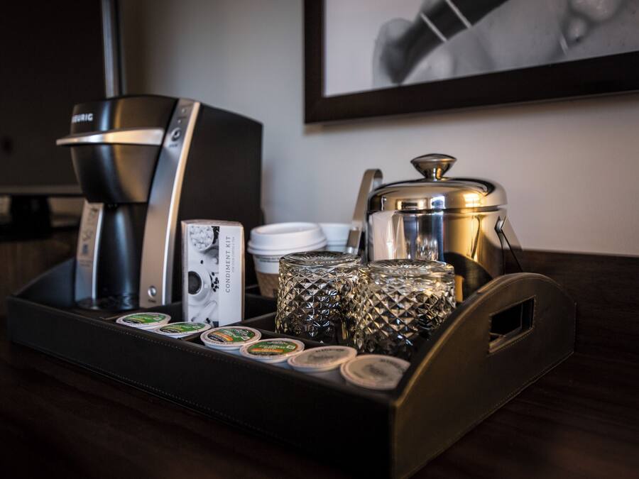 A coffee station with a coffee maker, cups, and condiments on a tray.