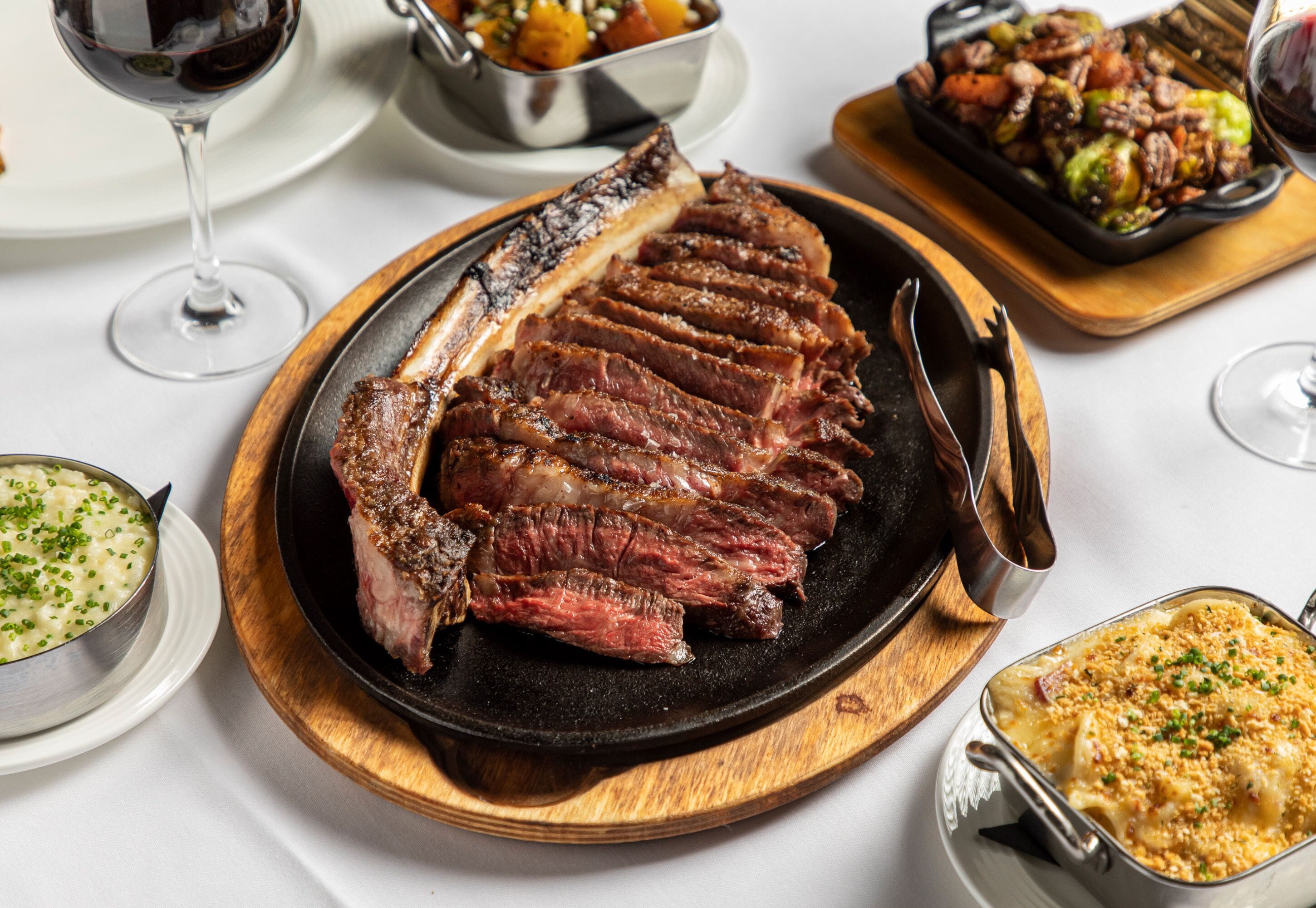 A steak with a black plate and a wooden board, accompanied by a bowl of soup and a dish of vegetables.