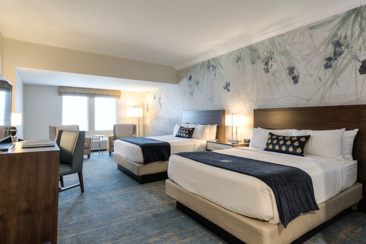Une chambre d’hôtel avec deux lits, un bureau, une chaise et une grande fenêtre.