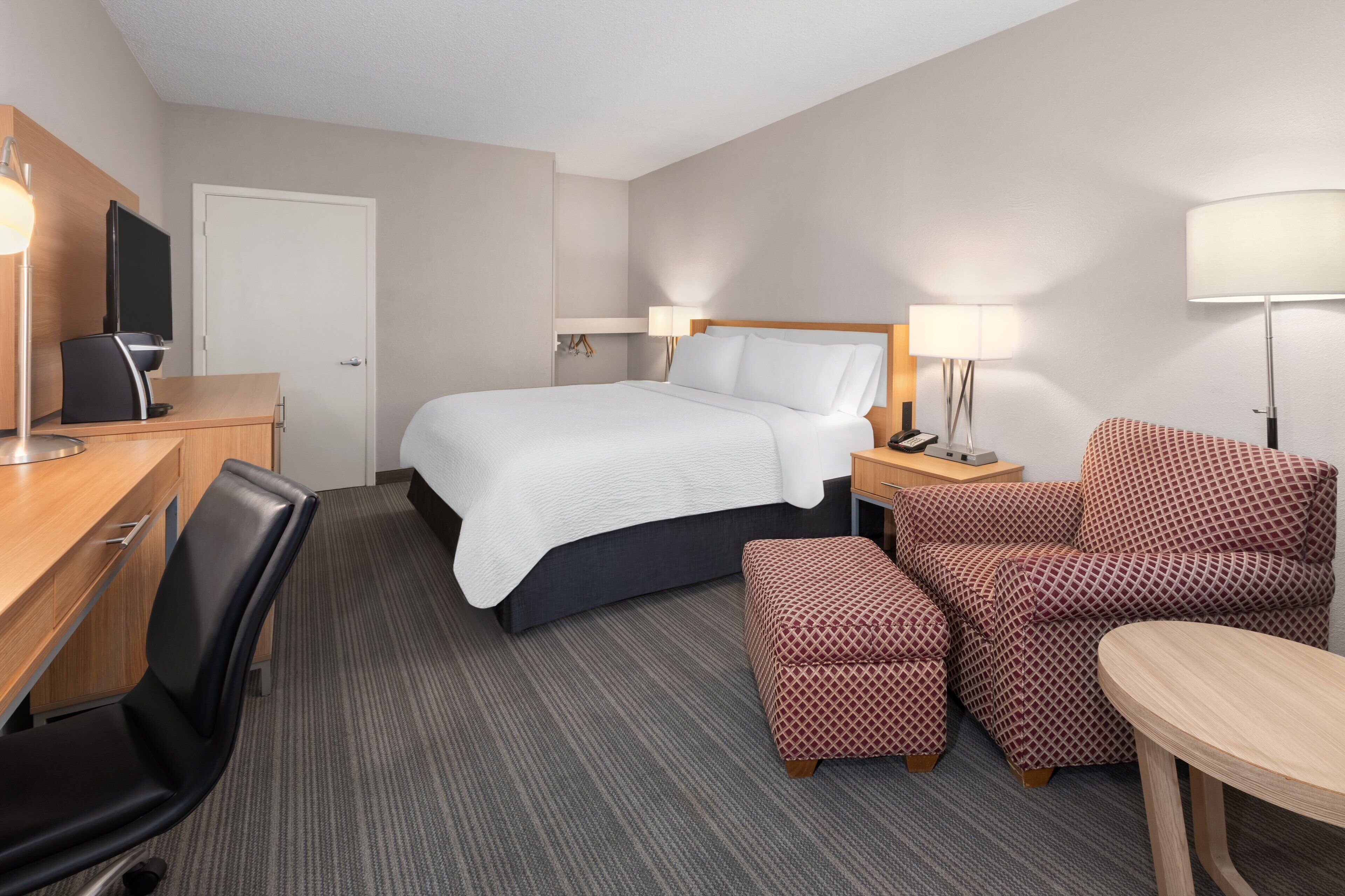 A hotel room with a bed, a desk with a computer, a chair, a sofa, and a table.