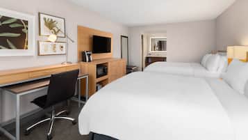Habitación de hotel con una cama grande, un escritorio con silla, televisor y cuadros con motivos botánicos en la pared.