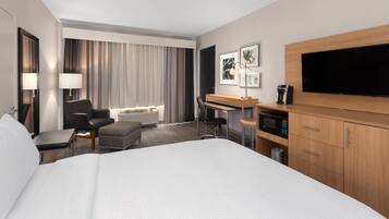 Una habitación de hotel con una cama grande, un escritorio con computadora, televisión y microondas.