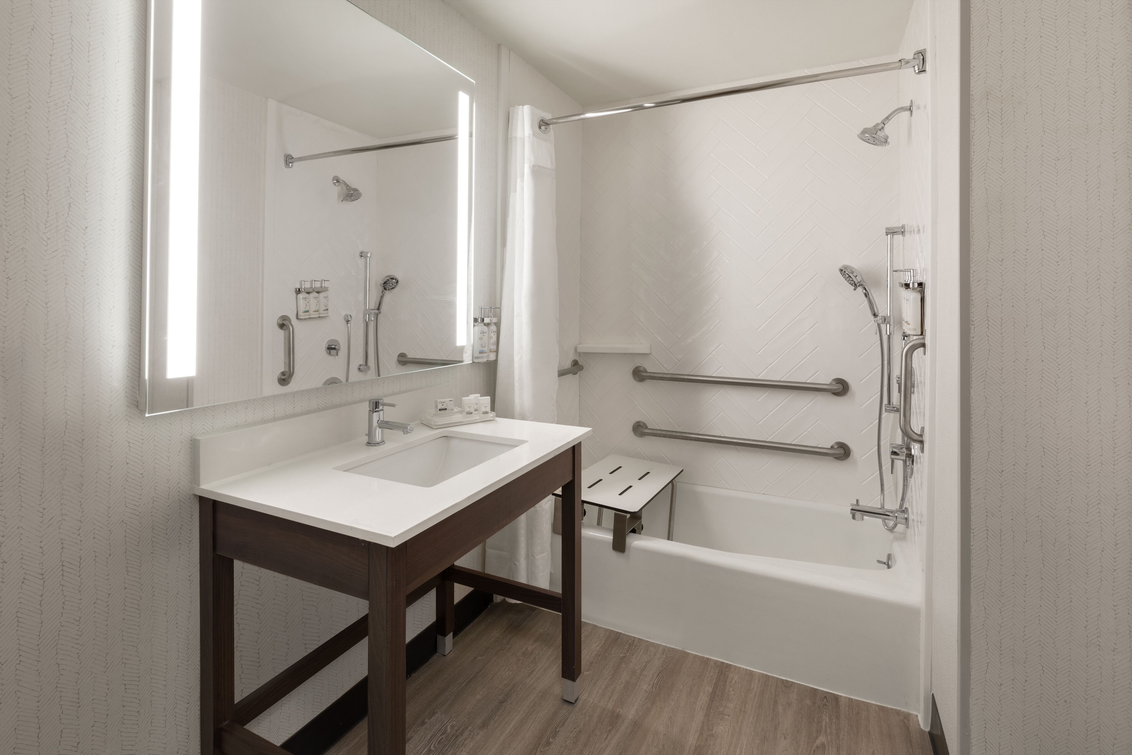 A modern bathroom with a double sink vanity, a bathtub with grab bars, and a shower with a handheld showerhead.