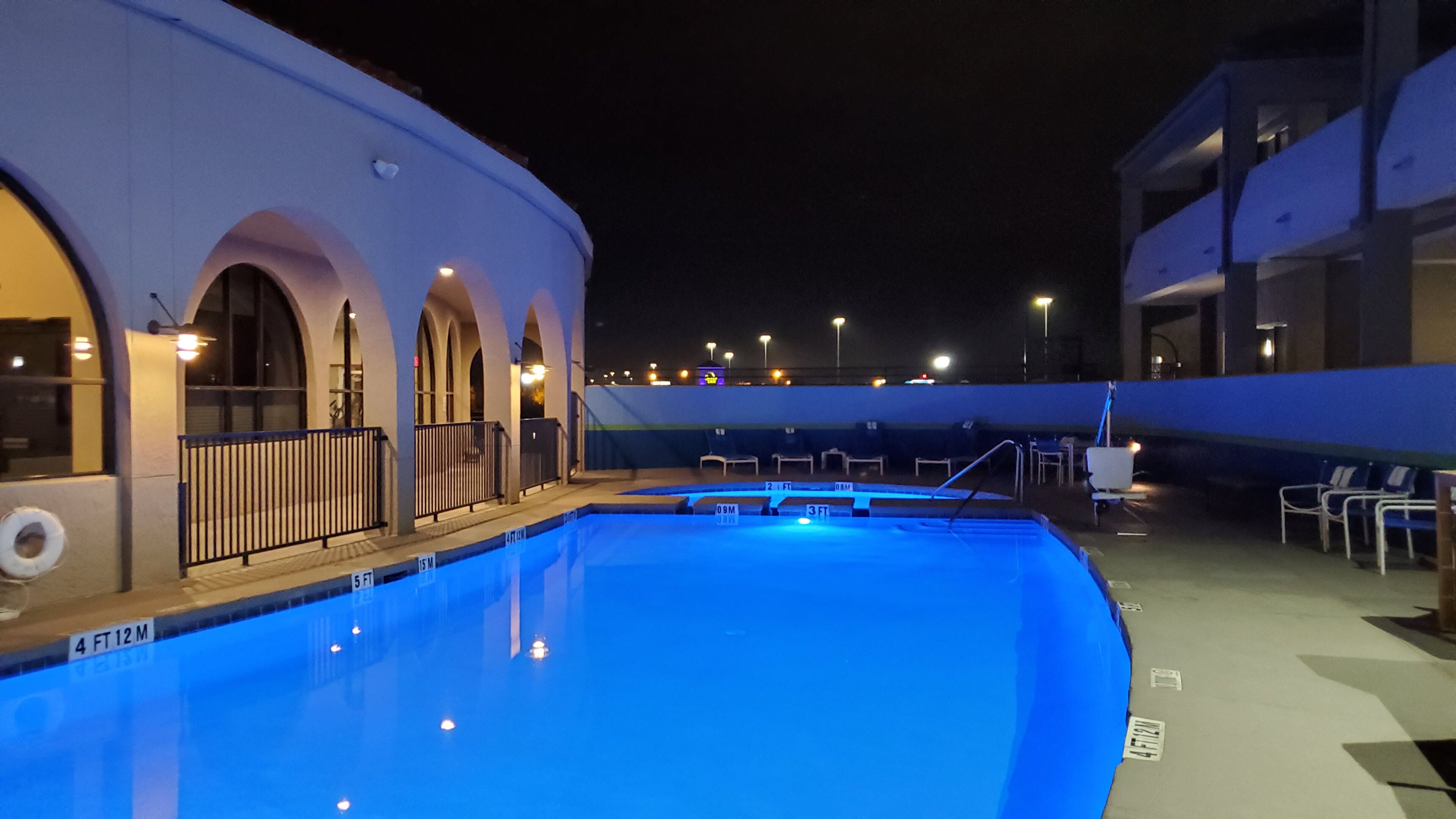 Una piscina de color azul, rodeada por un edificio con ventanas arqueadas y una barandilla.