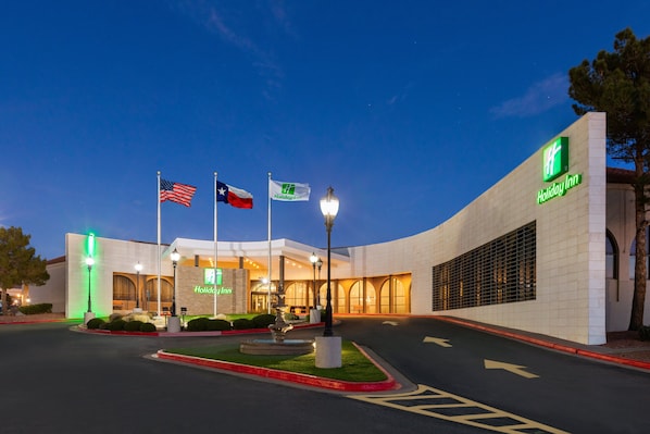 Un hôtel Holiday Inn au design moderne, caractérisé par un grand hall d’entrée, de nombreux drapeaux et une façade bien éclairée.