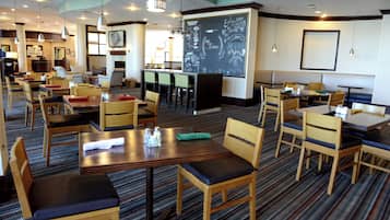 Un comedor de hotel con varias mesas y sillas, un menú en una pizarra y un mostrador de recepción al fondo.