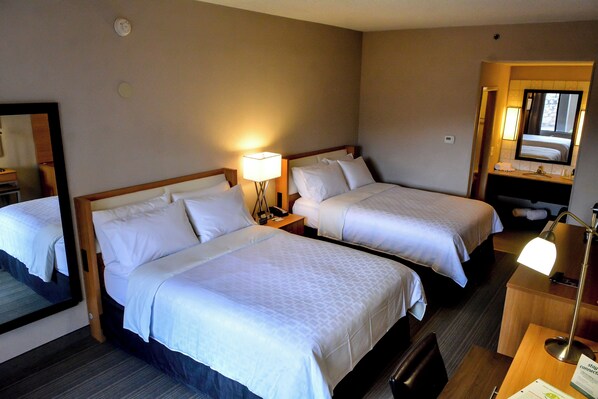 A hotel room with two beds, a bedside table with a lamp, a mirror, and a bathroom visible through an open door.
