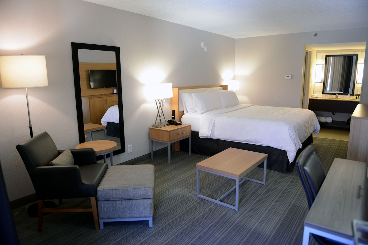 Ein Hotelzimmer mit Bett, Schreibtisch, Stuhl, kleinem Tisch, Spiegel und Fernseher.