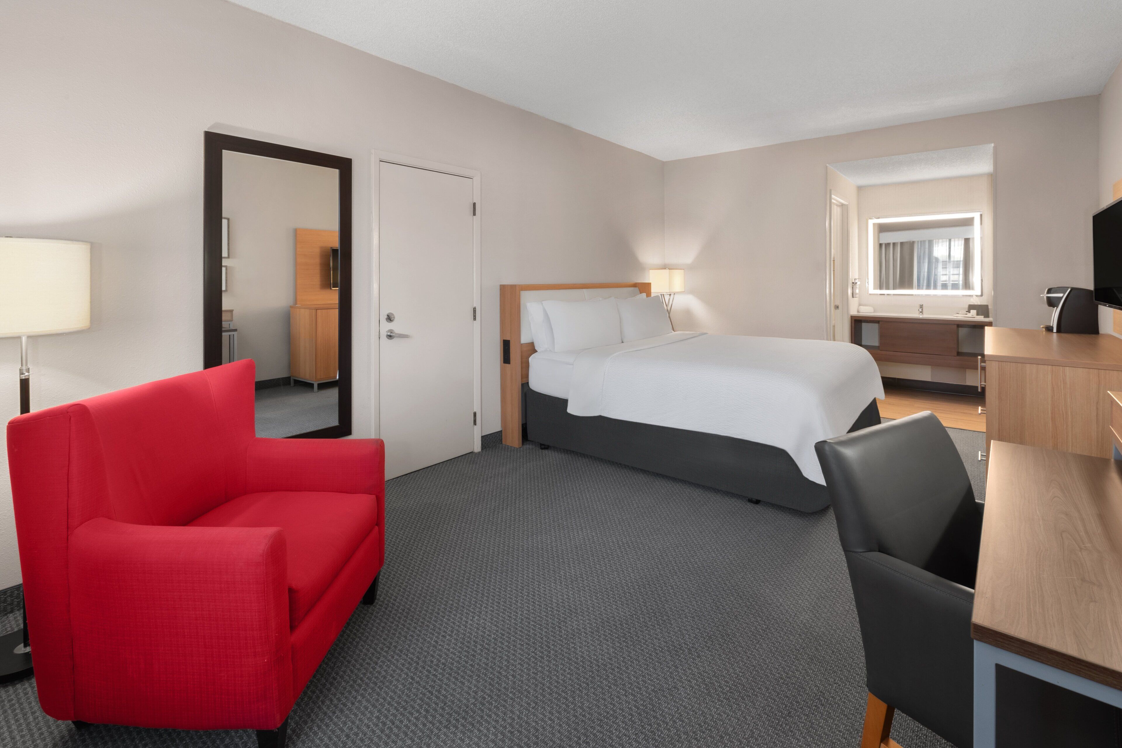 Ein Hotelzimmer mit Bett, Schreibtisch, Stuhl, rotem Ohrensessel und Spiegel.