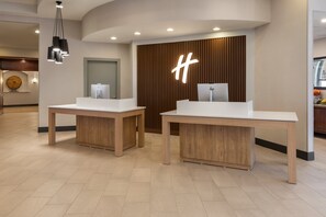 A reception area with two white reception desks, a wooden panel wall with a large illuminated 'H' logo, and a modern pendant light fixture.