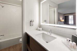 A modern bathroom with a large mirror, white sink, and shower.