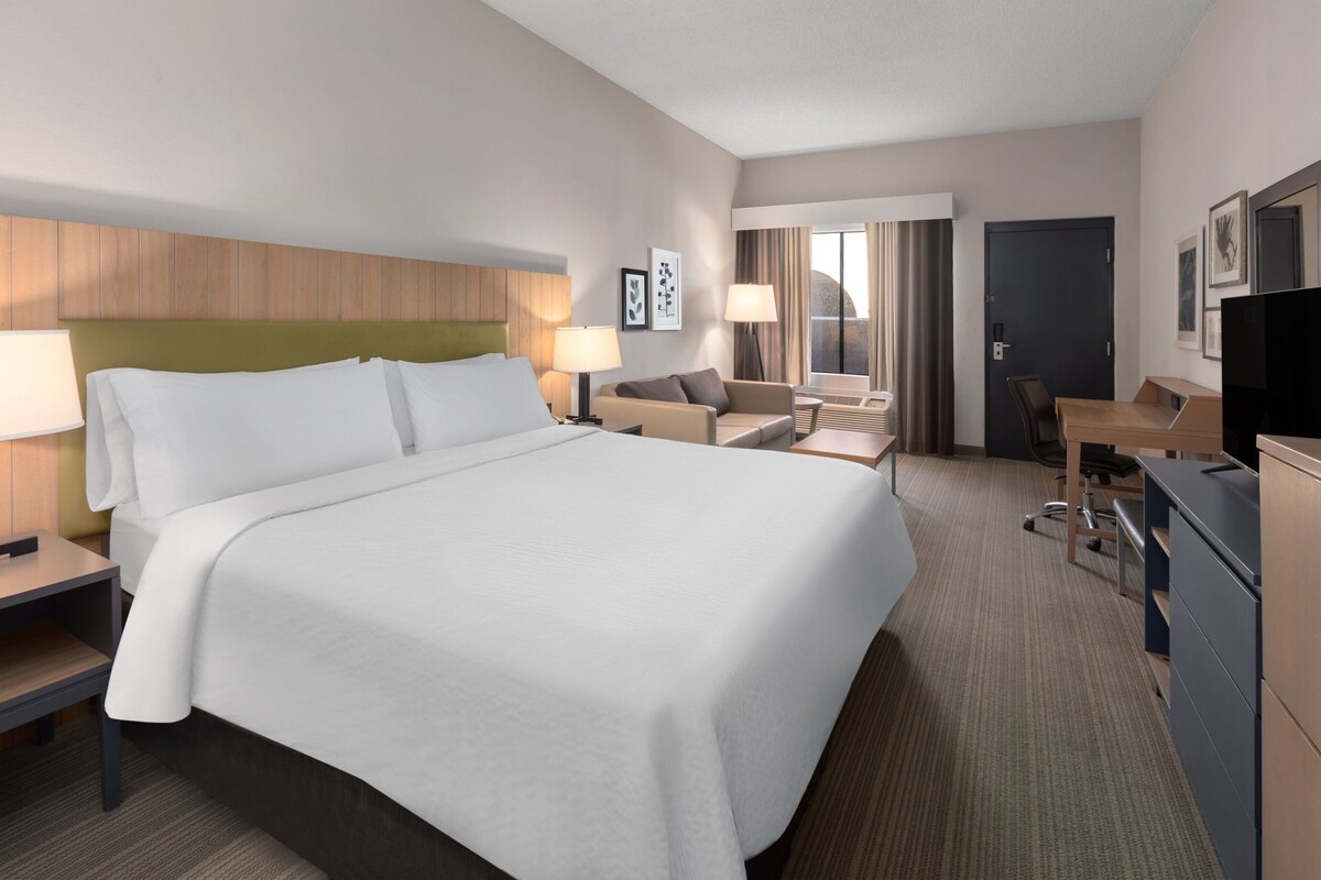 Une chambre d’hôtel avec un grand lit, un bureau, une chaise, une télévision et une fenêtre avec des rideaux.