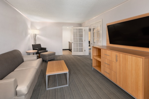 Ein modernes Hotelzimmer mit einer Couch, einem kleinen Tisch, einem Fernseher und einem Schrank.