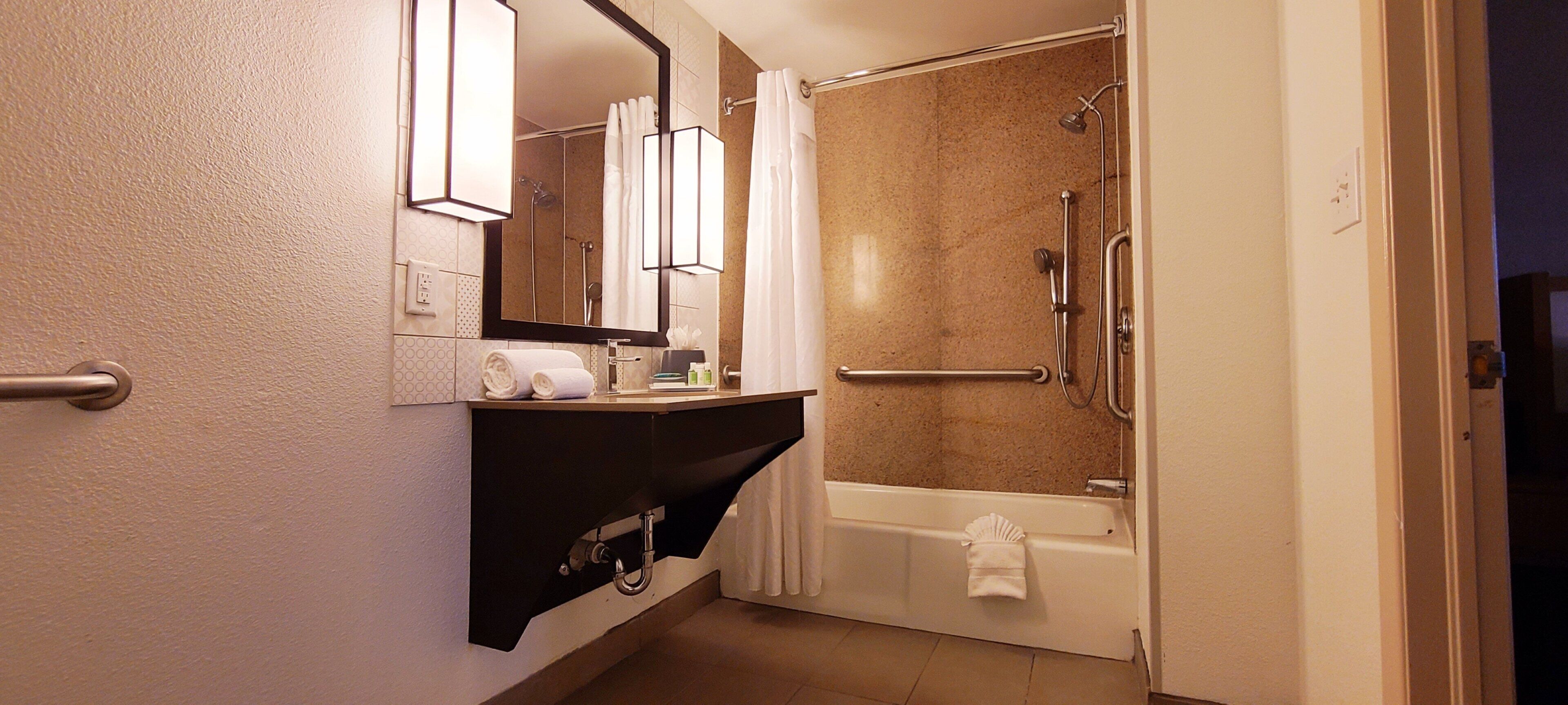 Un baño con ducha, bañera, lavabo con espejo y barra para toallas.